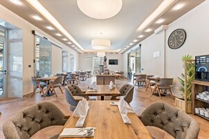 A modern hotel dining area with wooden tables, comfortable chairs, and a central bar.