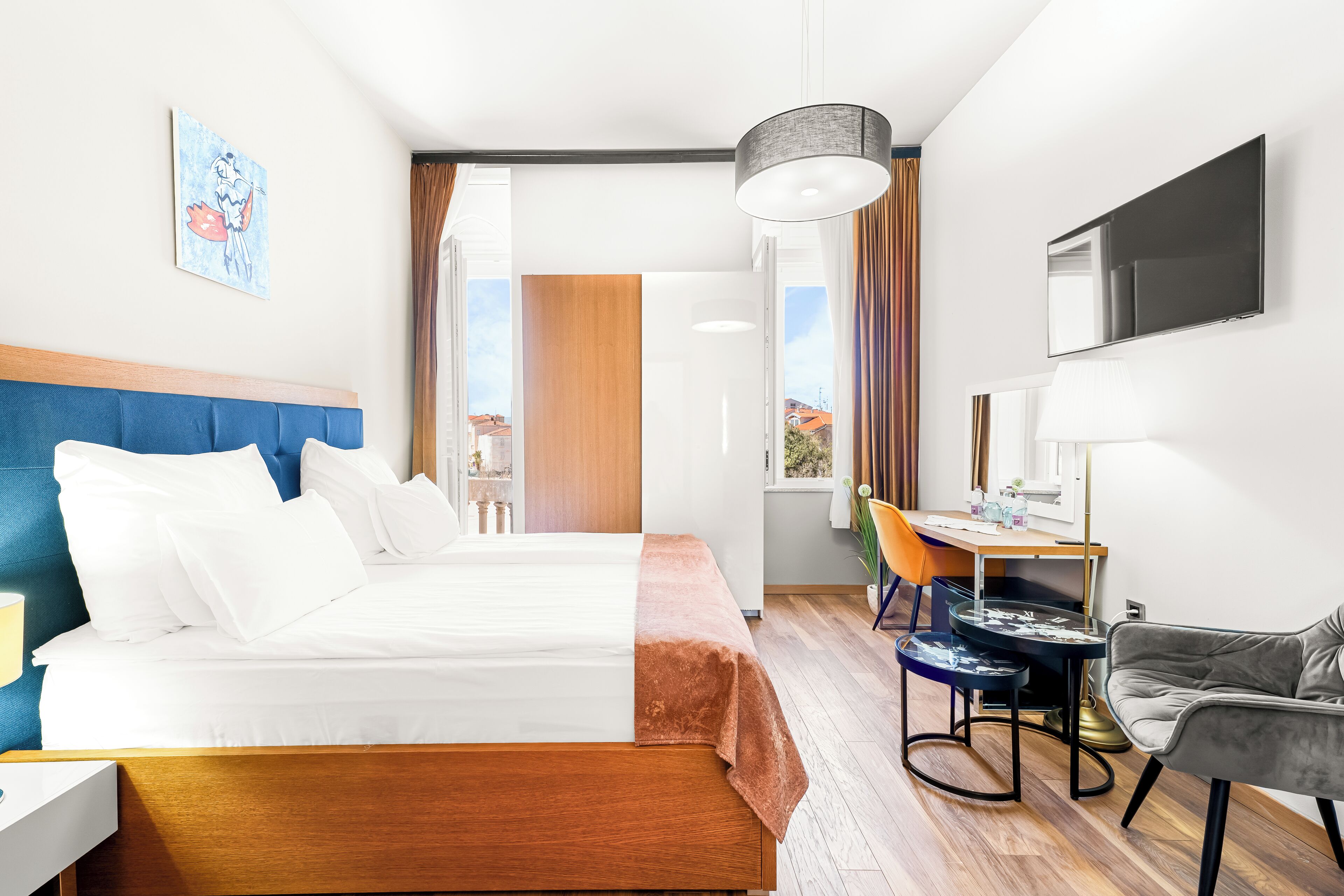 Habitación de hotel con cama, escritorio, silla, televisor y ventana.