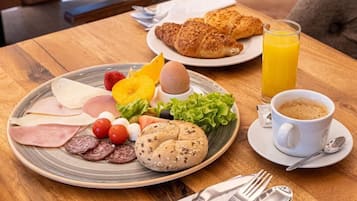 Een ontbijtsetting met een bord eten, croissants, sinaasappelsap en een kop koffie op een houten tafel.