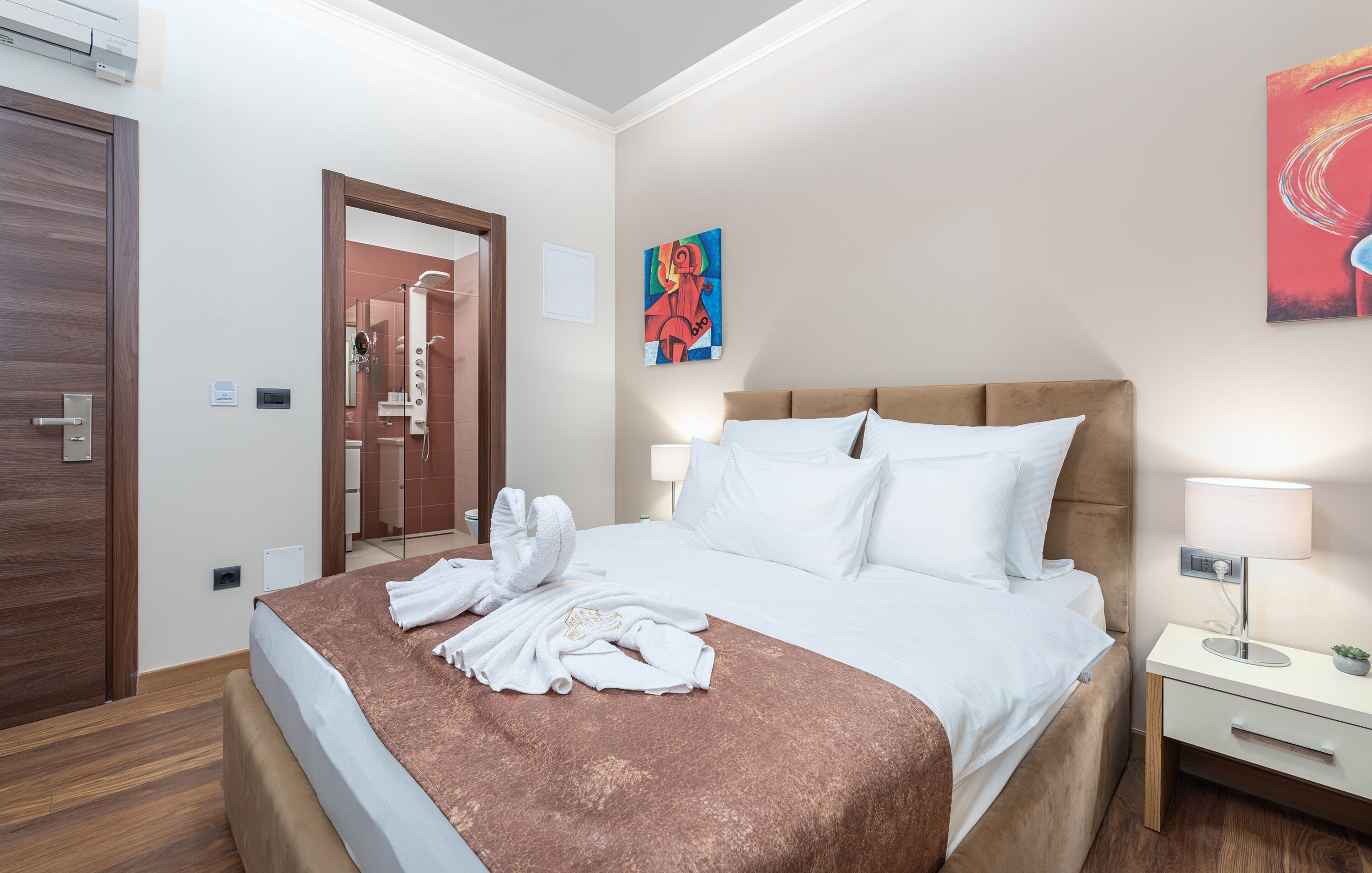 Una habitación de hotel con una cama, una mesita de noche, un cuadro en la pared y la puerta del baño.