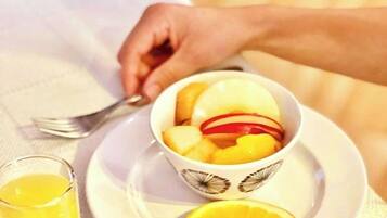 A bowl of fruit on a plate with a slice of orange beside it.