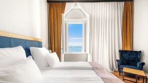 A hotel room with a large bed, a chair, and a view of the sea through an open window. - Hotel Dua Residence (Porec)