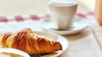 Een croissant op een bord, een kop koffie en een glas melk op een tafel met een geruit tafelkleed.