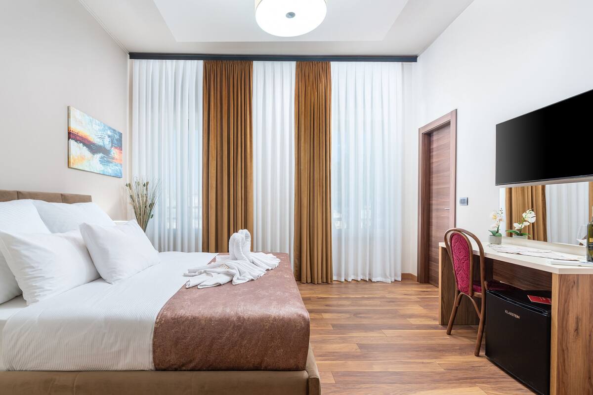 A hotel room with a bed, a desk, a TV, and curtains.
