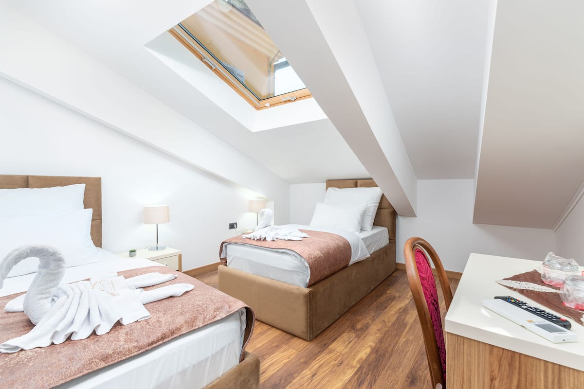 A modern hotel room with two beds, a skylight, wooden flooring, and a small table with a remote control.