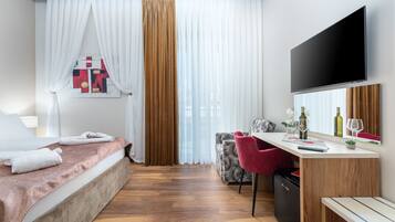 Una habitación de hotel moderna con una cama, un escritorio con silla, un televisor y una ventana con cortinas.