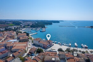Vista aérea de un pueblo costero con edificios históricos, un puerto deportivo y un mar azul cristalino.