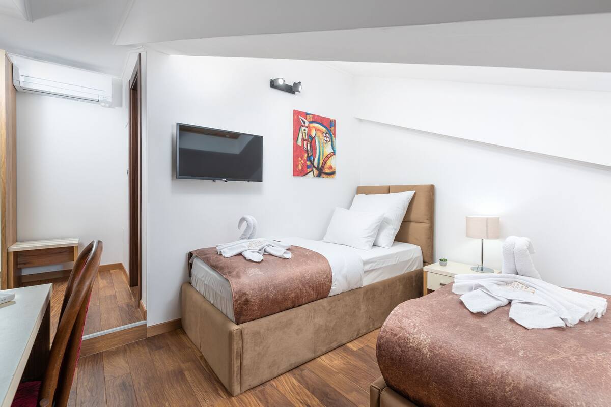 A hotel room with two beds, a TV, a painting, a desk, and a chair.