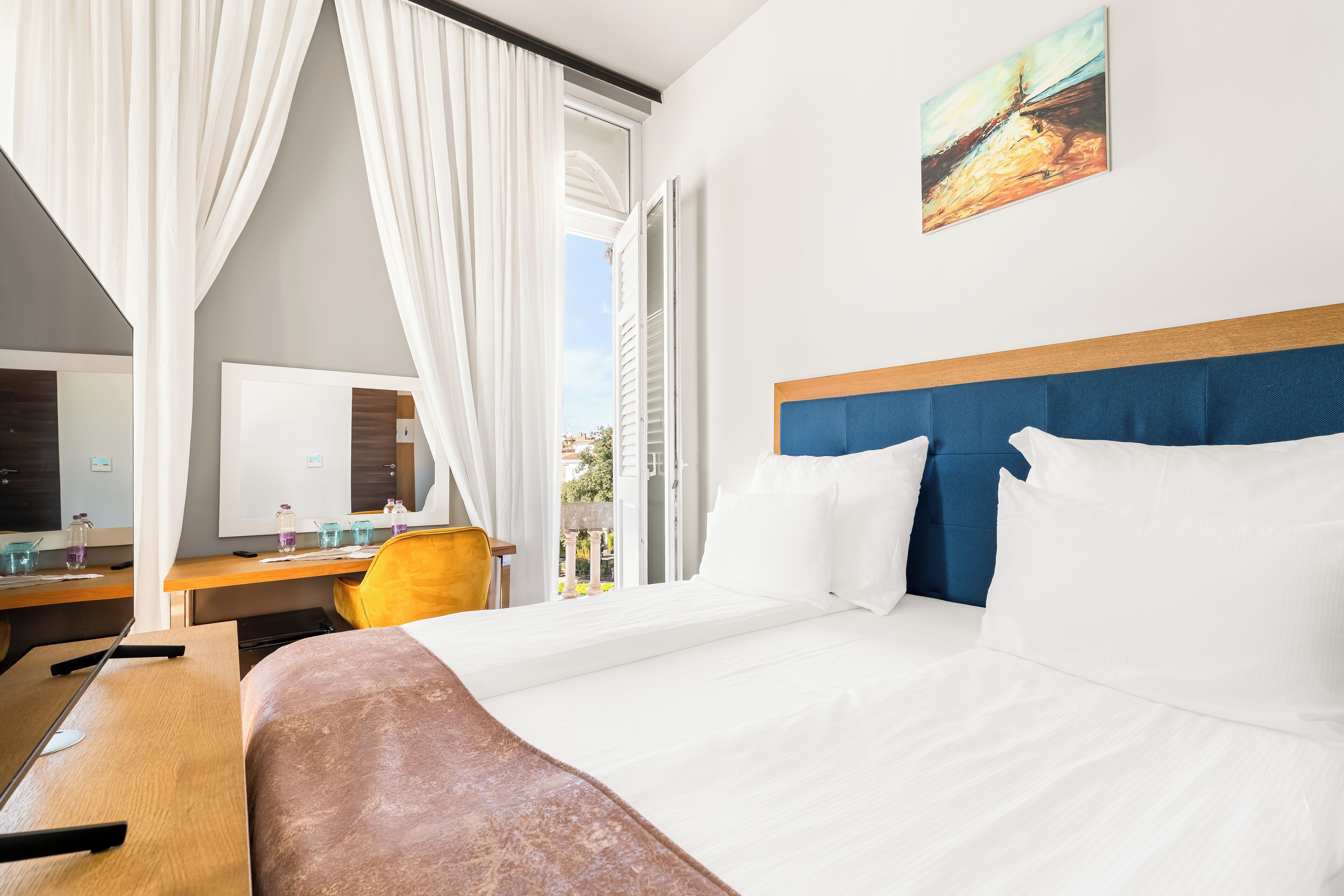 A hotel room with a bed, a desk, a chair, and a window with curtains.