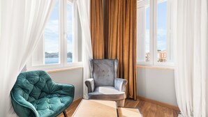 A room with a teal armchair, a grey armchair, a wooden table, and large windows with curtains. - Hotel Dua Residence (Porec)