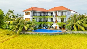 A two-story building with a swimming pool, surrounded by lush greenery and palm trees. - Sunkissed Paddy Hoi An Villa (Da Nang)