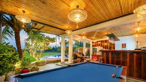 A pool table with a wooden ceiling and hanging lights, surrounded by potted plants and a view of a pool. - Sunkissed Paddy Hoi An Villa (Da Nang)