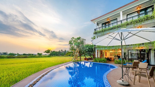 A swimming pool with a wooden deck, surrounded by lush greenery and a view of a rice field. - Sunkissed Paddy Hoi An Villa (Da Nang)
