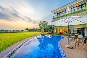 Piscina com deck de madeira, cercada por vegetação exuberante e vista para um campo de arroz.