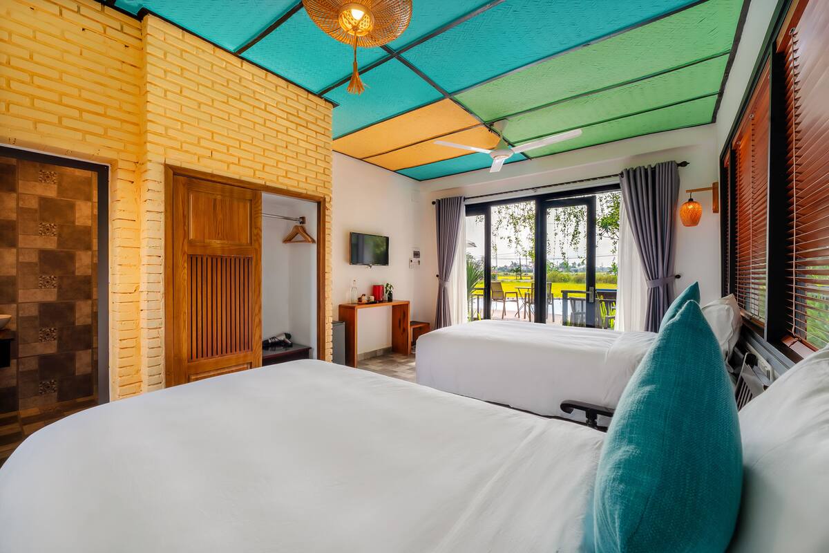 Ein Hotelzimmer mit zwei Betten, einer Holztür, einem Fernseher und einem Balkon mit Blick.
