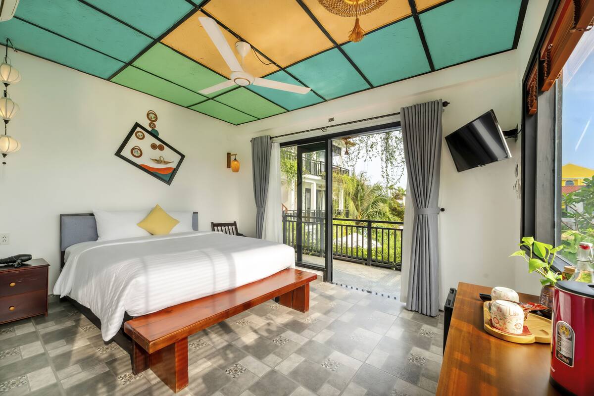 Ein Schlafzimmer mit Bett, Bank, Nachttisch, Deckenventilator und Blick auf den Balkon.