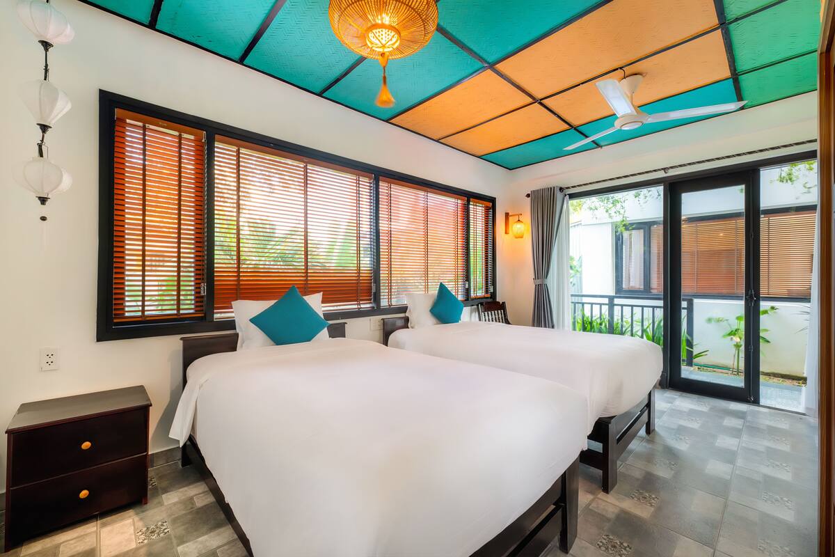 Ein Hotelzimmer mit zwei Betten, einem Deckenventilator und großen Fenstern mit Jalousien.