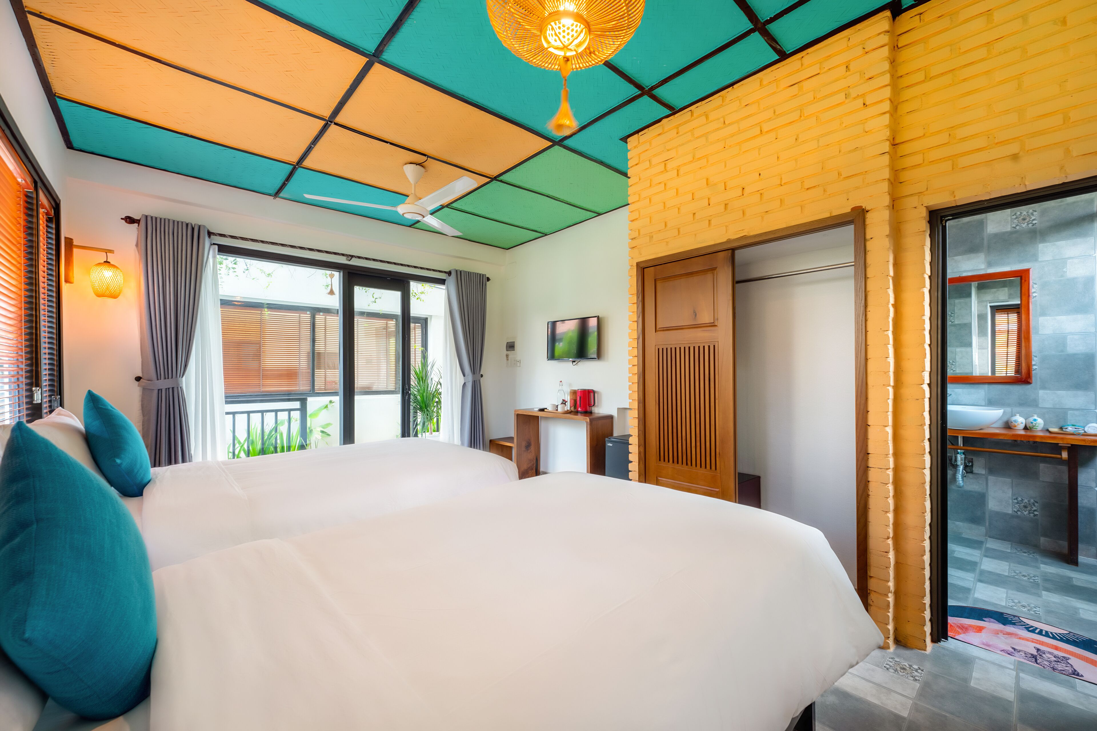 A hotel room with a large bed, a ceiling fan, a TV, and a bathroom with a sink and mirror.