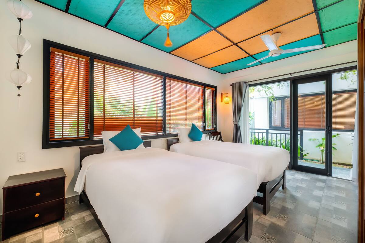 Ein Hotelzimmer mit zwei Betten, einem Deckenventilator und großen Fenstern mit Jalousien.