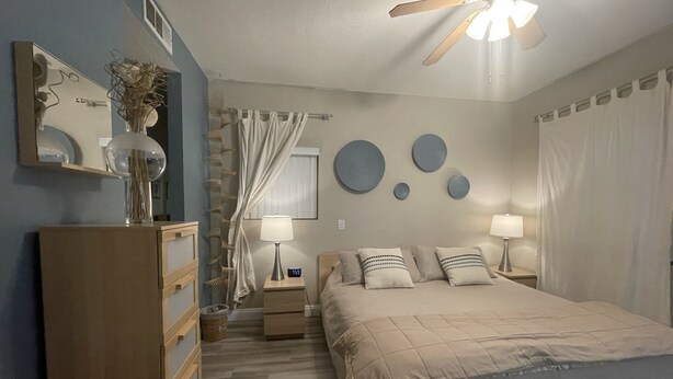 A bedroom with a bed, bedside tables, a mirror, a ceiling fan, and wall decorations.