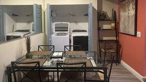 A compact kitchen with a built-in oven and microwave, a dining area with a glass table and chairs, and a red accent wall.