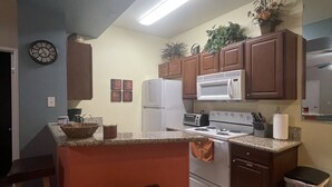 A kitchen with a central island, wooden stools, a refrigerator, a microwave, and a stove.
