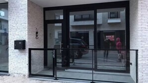 Entrada de un edificio con puertas de vidrio, barandilla de metal negro y un coche estacionado afuera.