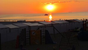 Una playa con un atardecer, un parque infantil y una hilera de cabañas de playa.