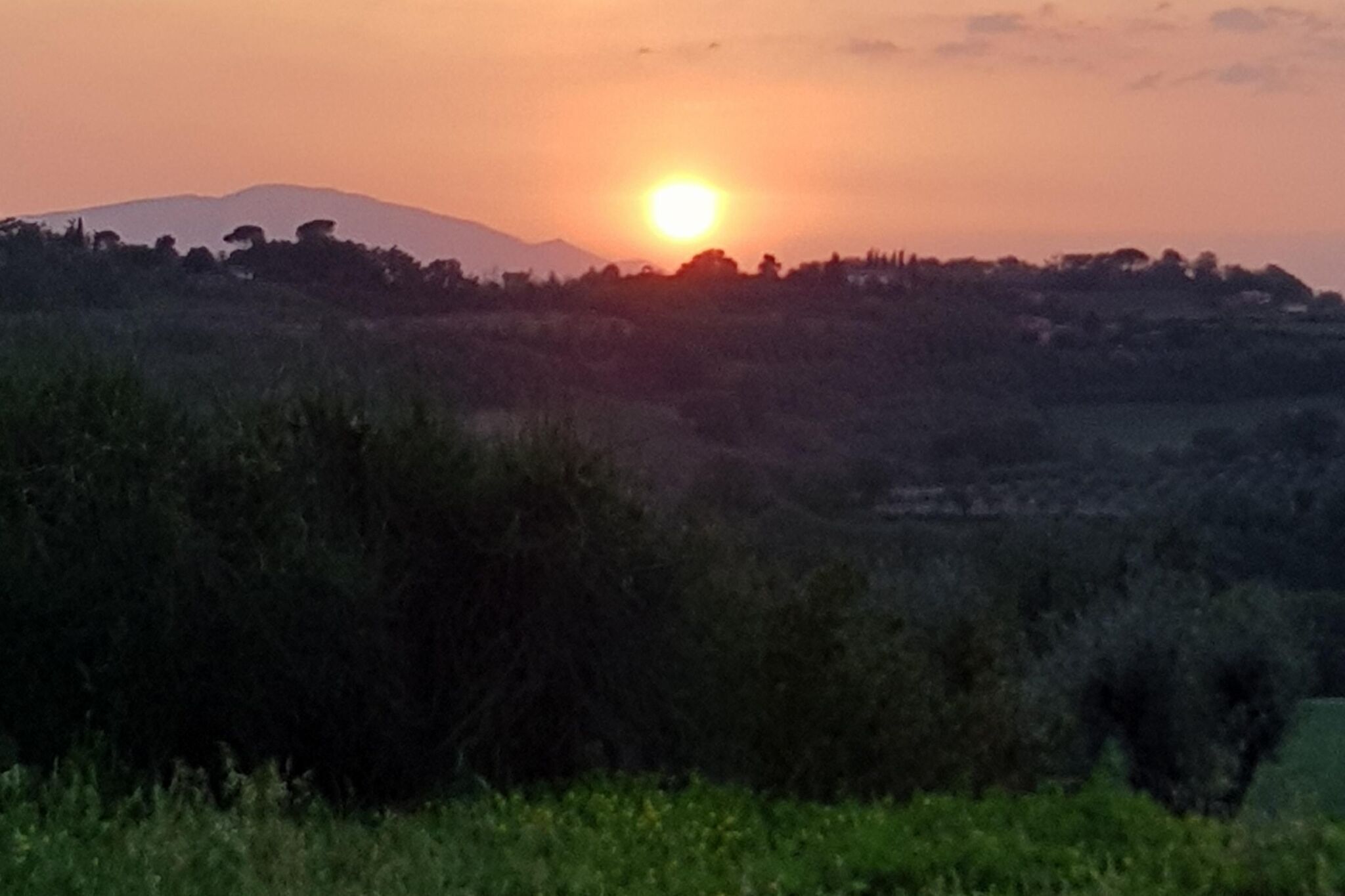 Een zonsondergang boven een glooiend landschap met een heldere lucht.