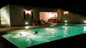 A swimming pool area with a staircase leading to an upper level, lounge chairs, and a well-lit interior. - Belvilla by OYO Villa Roma Sabina (Borgonuovo)