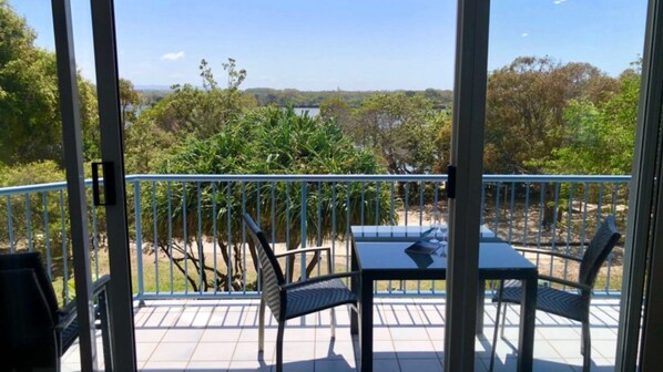 A balcony with a table and chairs, overlooking a natural landscape with trees and a body of water.