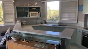 Een moderne keuken met een glazen kookeiland, een ingebouwde magnetron en uitzicht op groen.