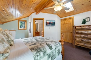 A bedroom with a bed, wooden ceiling, a dresser, a door, and a window.