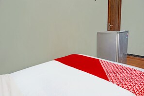Una habitación con una cama, un refrigerador pequeño y una puerta de madera.