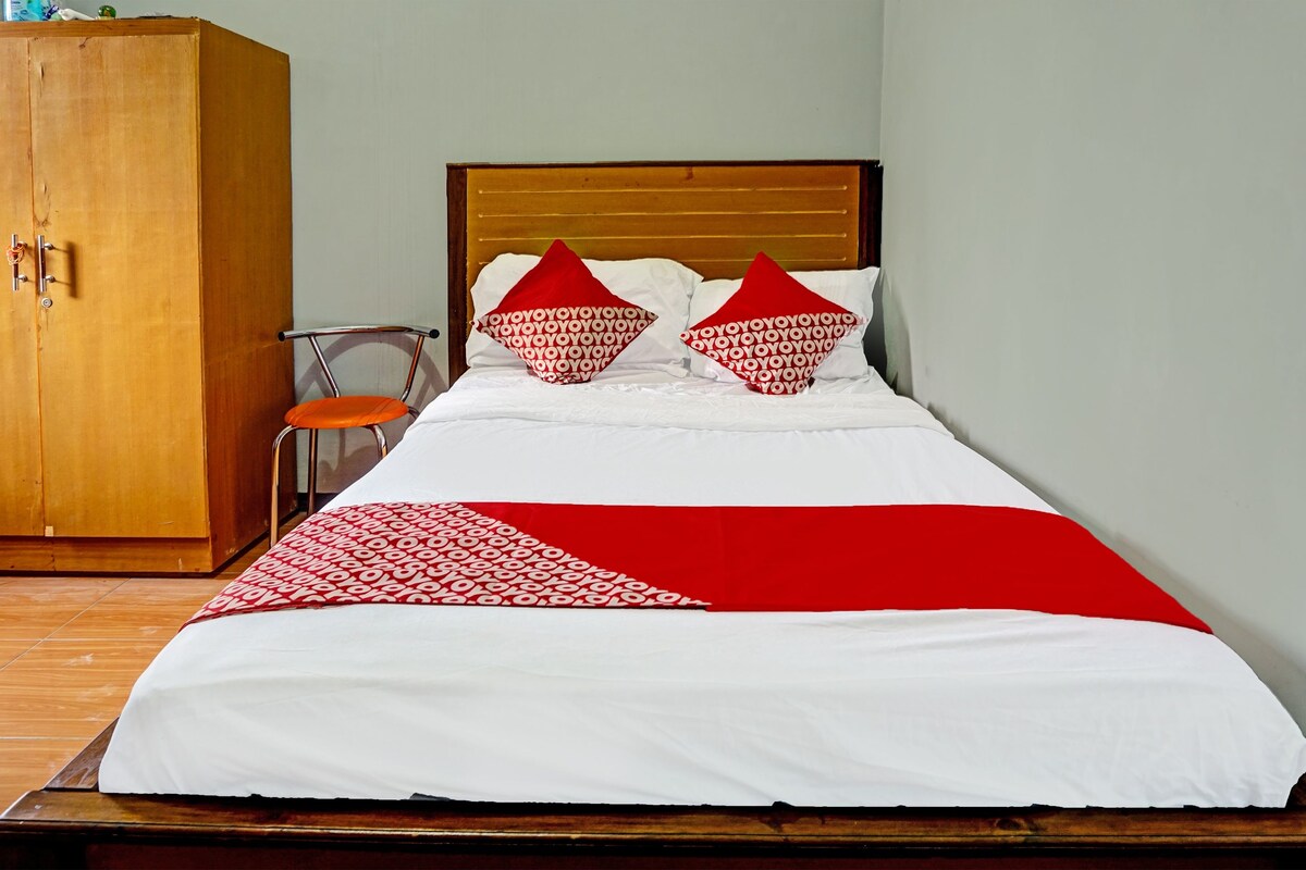 Un lit recouvert d’une couvre-lit rouge et blanche, deux oreillers rouges, une tête de lit en bois et une armoire en bois.