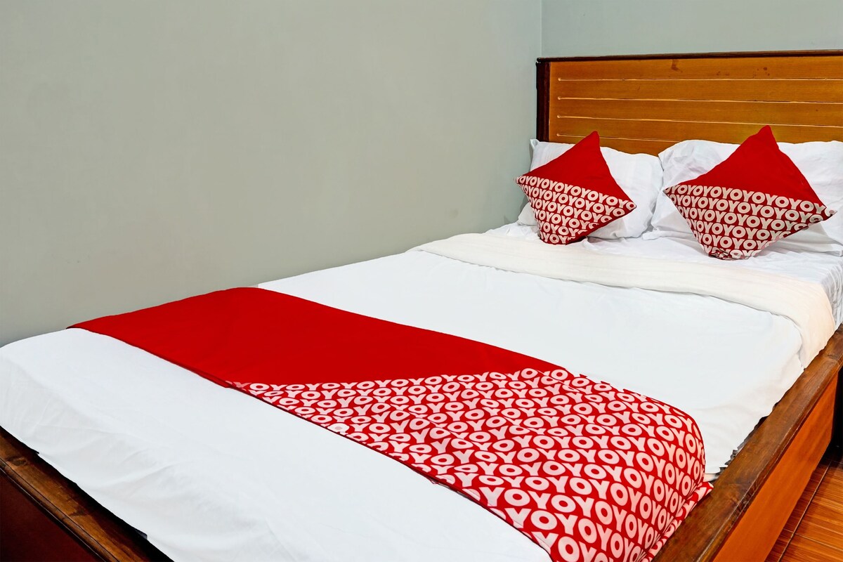 Un lit avec une tête de lit en bois, une literie blanche et des coussins à motifs rouges et blancs.