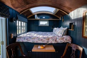 A cozy room with a bed, a small table with a bowl, and a window.
