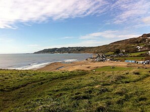A coastal landscape with a beach, grassy areas, and a small settlement with buildings and vehicles.