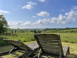 Two wooden lounge chairs in a grassy field with a clear sky.