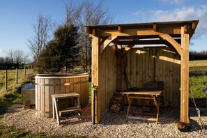 A wooden outdoor structure with a bench, a table, and a hot tub.