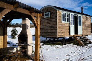 A wooden cabin with a small porch and a fireplace, situated on a snowy landscape.