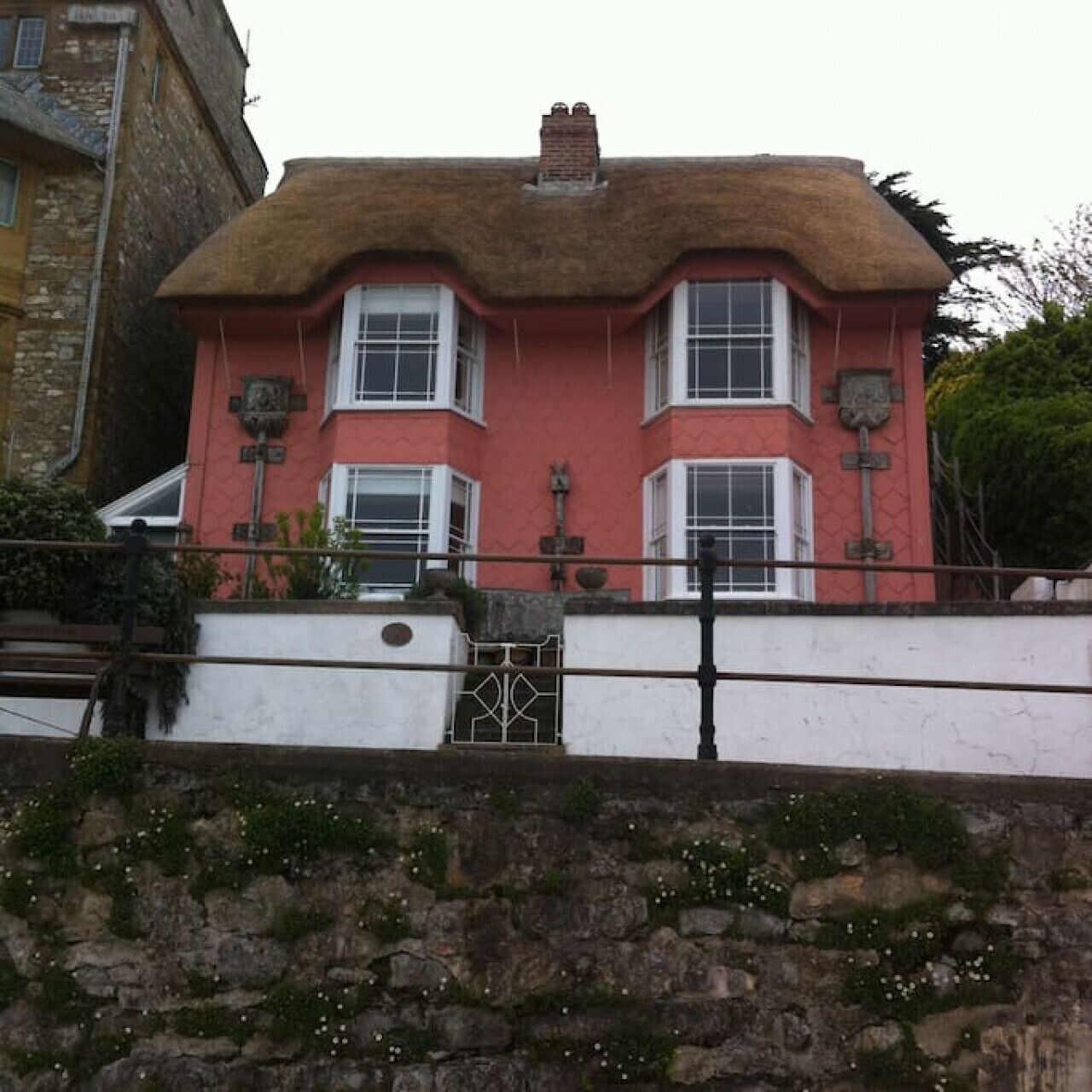 A two-story building with a red facade, white window frames, and a thatched roof.