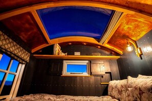 A room with a sloped ceiling, a window, a bed, and a small TV.