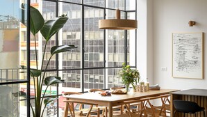 Een moderne woonkamer met een bank, eettafel, stoelen, een potplant en een groot raam met uitzicht op de stad.