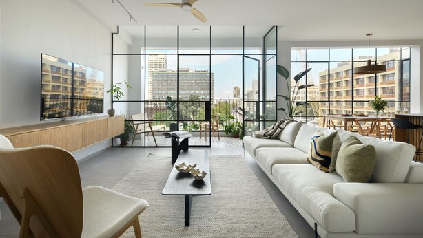 Een moderne woonkamer met een witte bank, een houten stoel, een salontafel en een groot raam met uitzicht op de stad.
