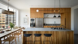 Een moderne keuken met een centraal eiland, houten keukenkastjes en barstoelen.