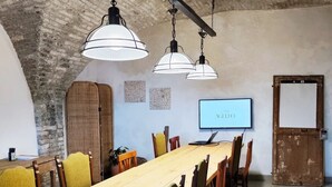 A conference room with a long table, chairs, hanging pendant lights, a television, and a whiteboard. - Casa Agello B&B (Ripatransone)