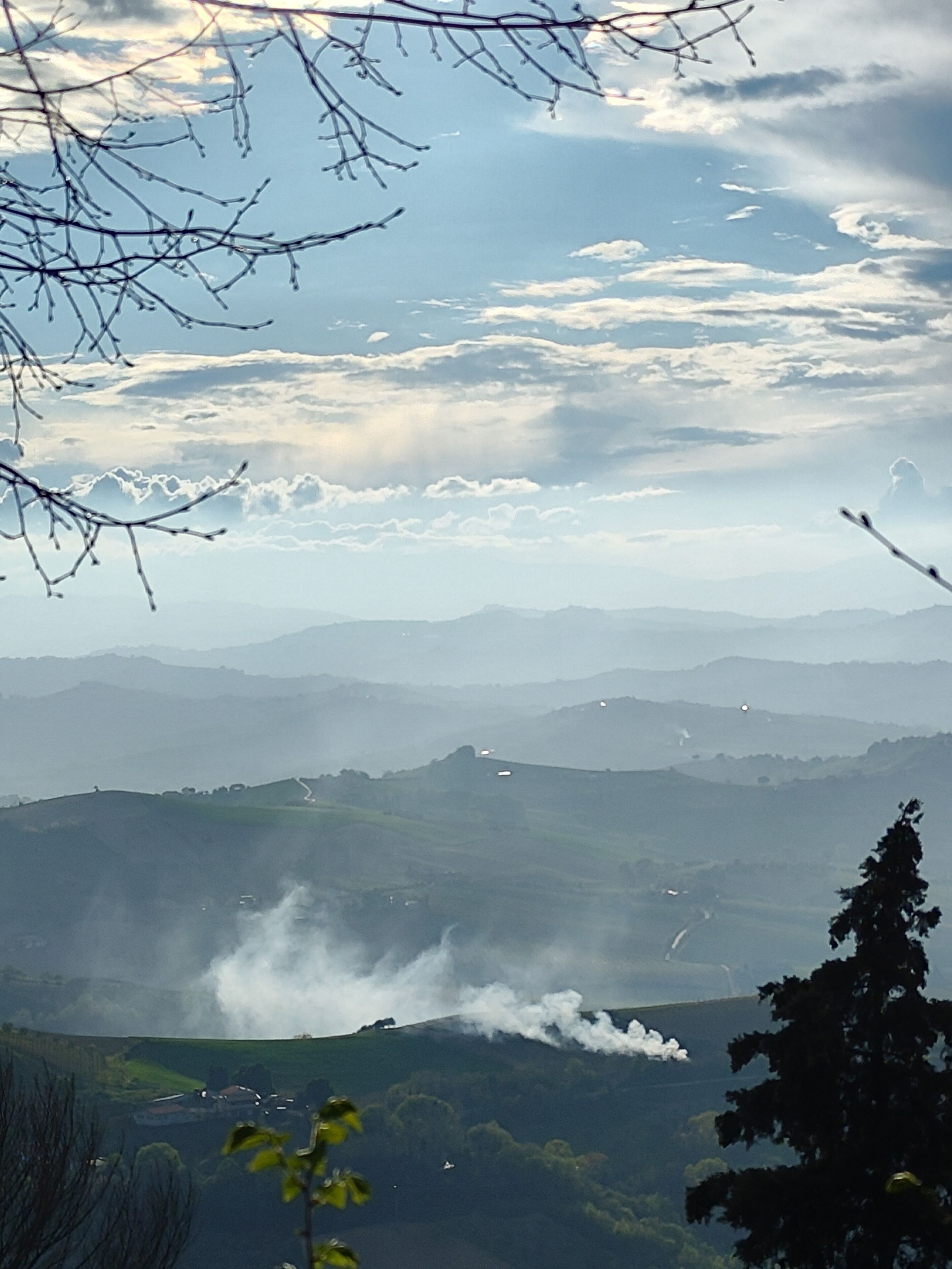 Un paisaje montañoso con una carretera serpenteando por los valles. Humo se eleva desde una colina distante, lo que sugiere posible actividad industrial.