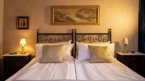 A double bed with two nightstands, each with a lamp, a framed portrait, and a painting on the wall. - Casa Agello B&B (Ripatransone)