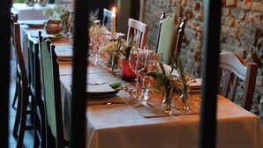 A dining area with a stone wall, a table set with glassware and flowers, and a candle on the table. - Casa Agello B&B (Ripatransone)